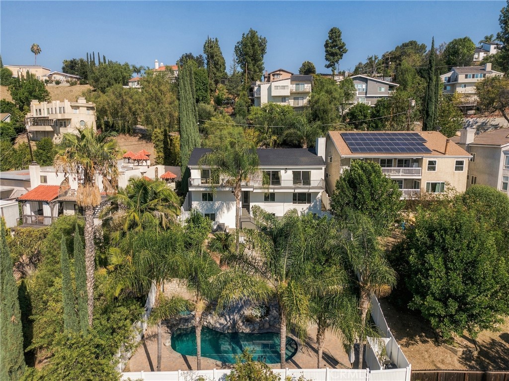 Aerial view of a home with a backyard pool, palm trees, and rooftop solar panels.