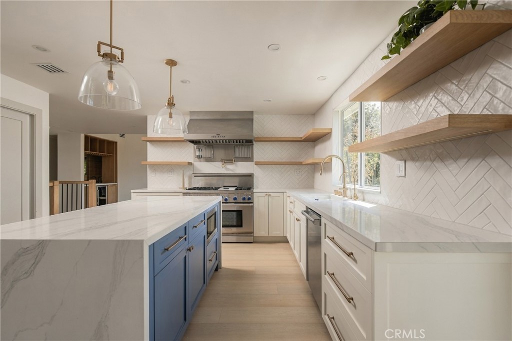 Kitchen with a marble island, blue cabinetry, brass fixtures, and floating wood shelves.