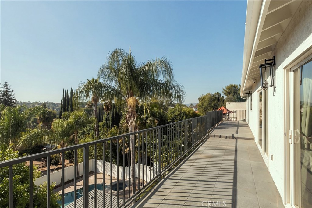Upper-level balcony with gray tile, black railing, palm trees, and a partial view of the pool.
