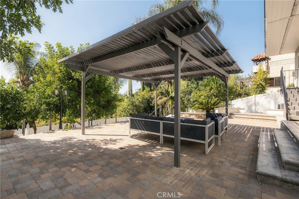 Outdoor patio with a metal pergola shading a sectional seating area on stone pavers.