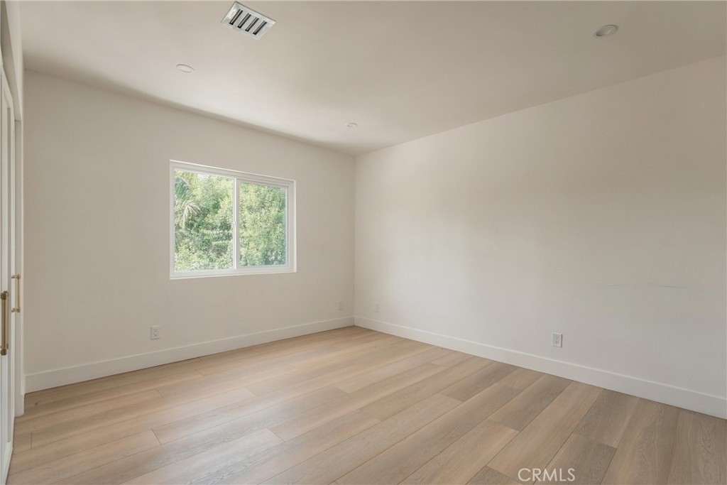 Empty room with light plank flooring and a window overlooking greenery.