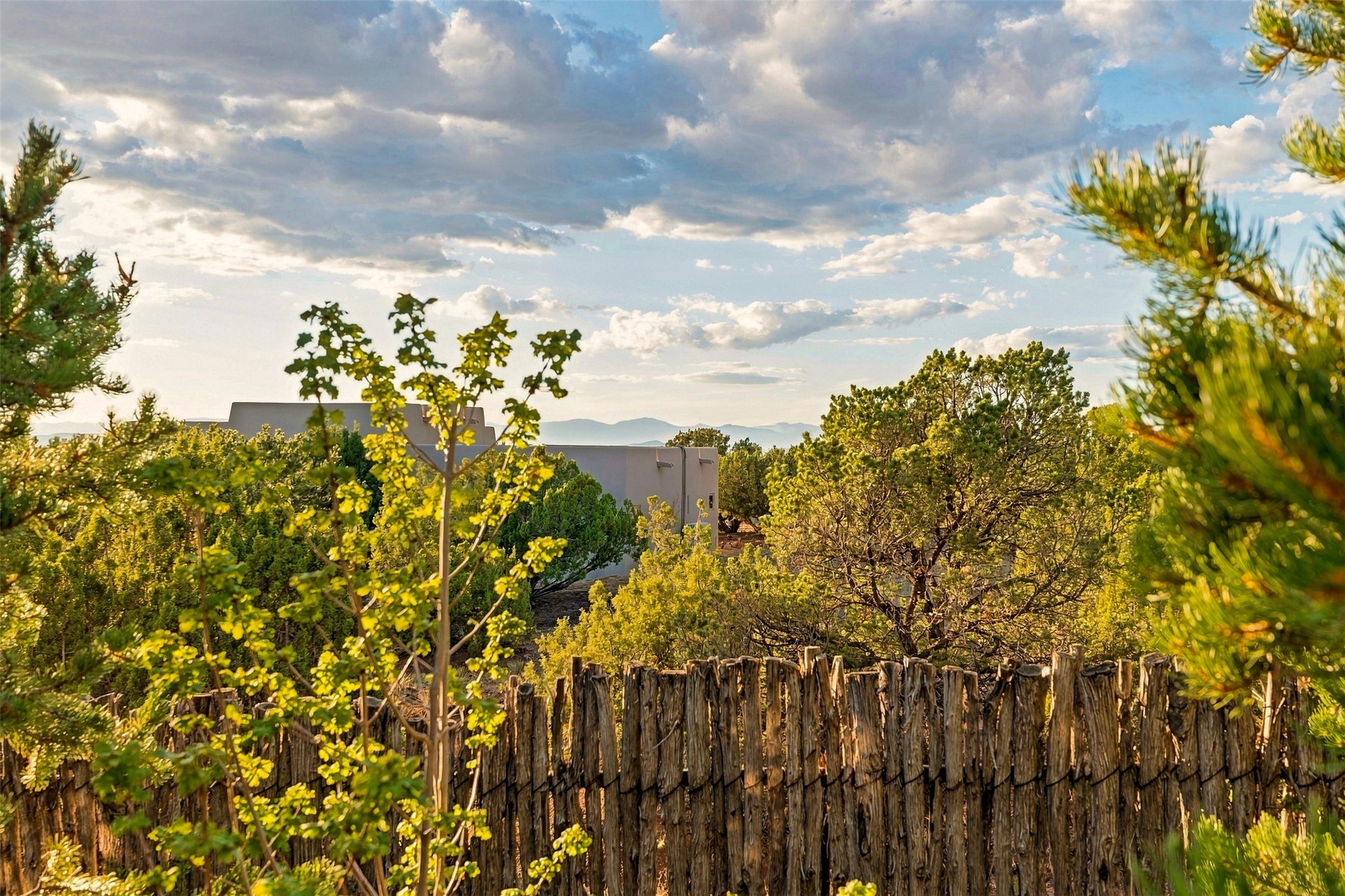Modern home among trees behind a rustic wood fence, with distant mountain ridges.