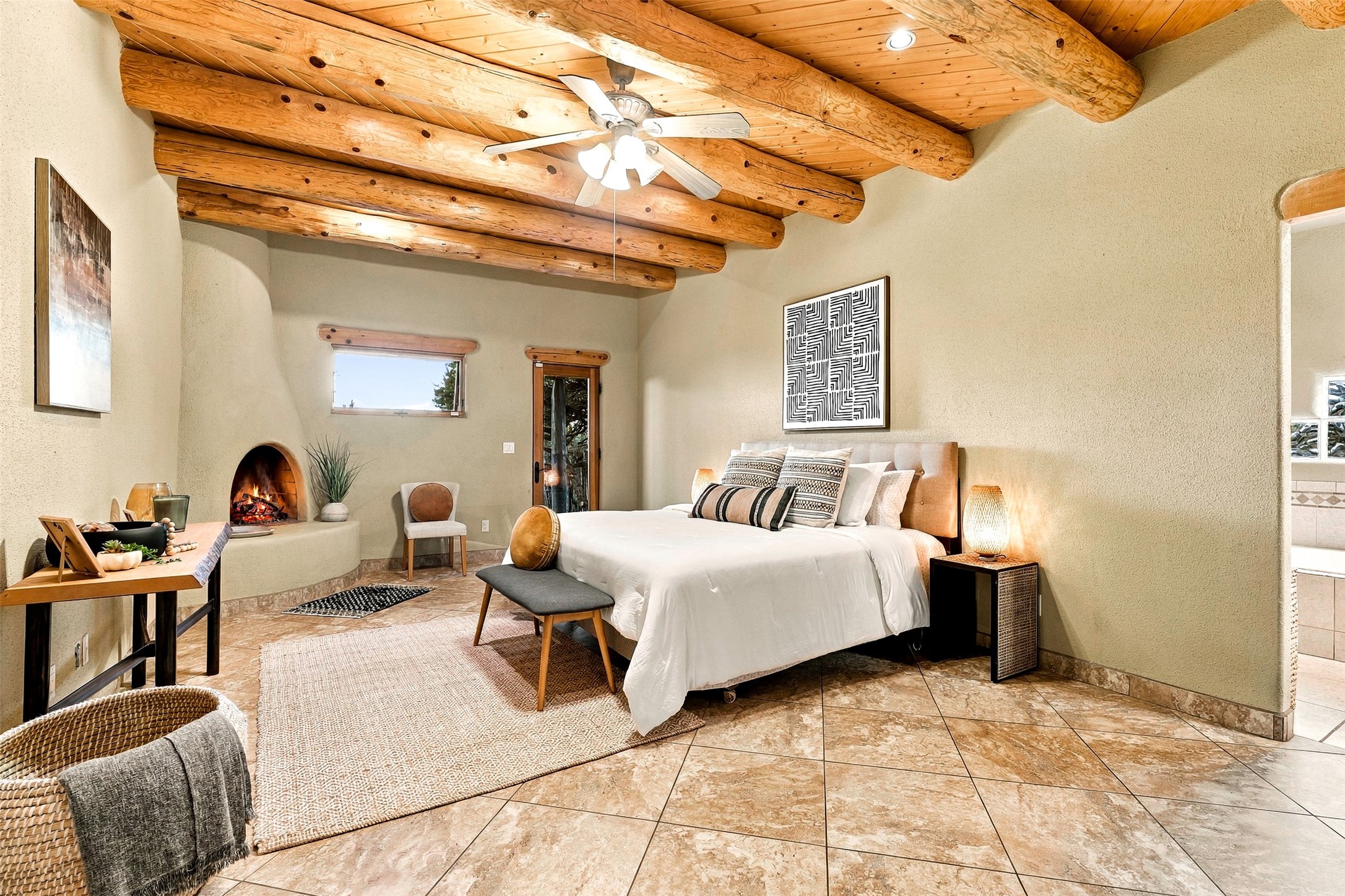 Bedroom with exposed wooden beams, a king bed, and a lit kiva-style fireplace.