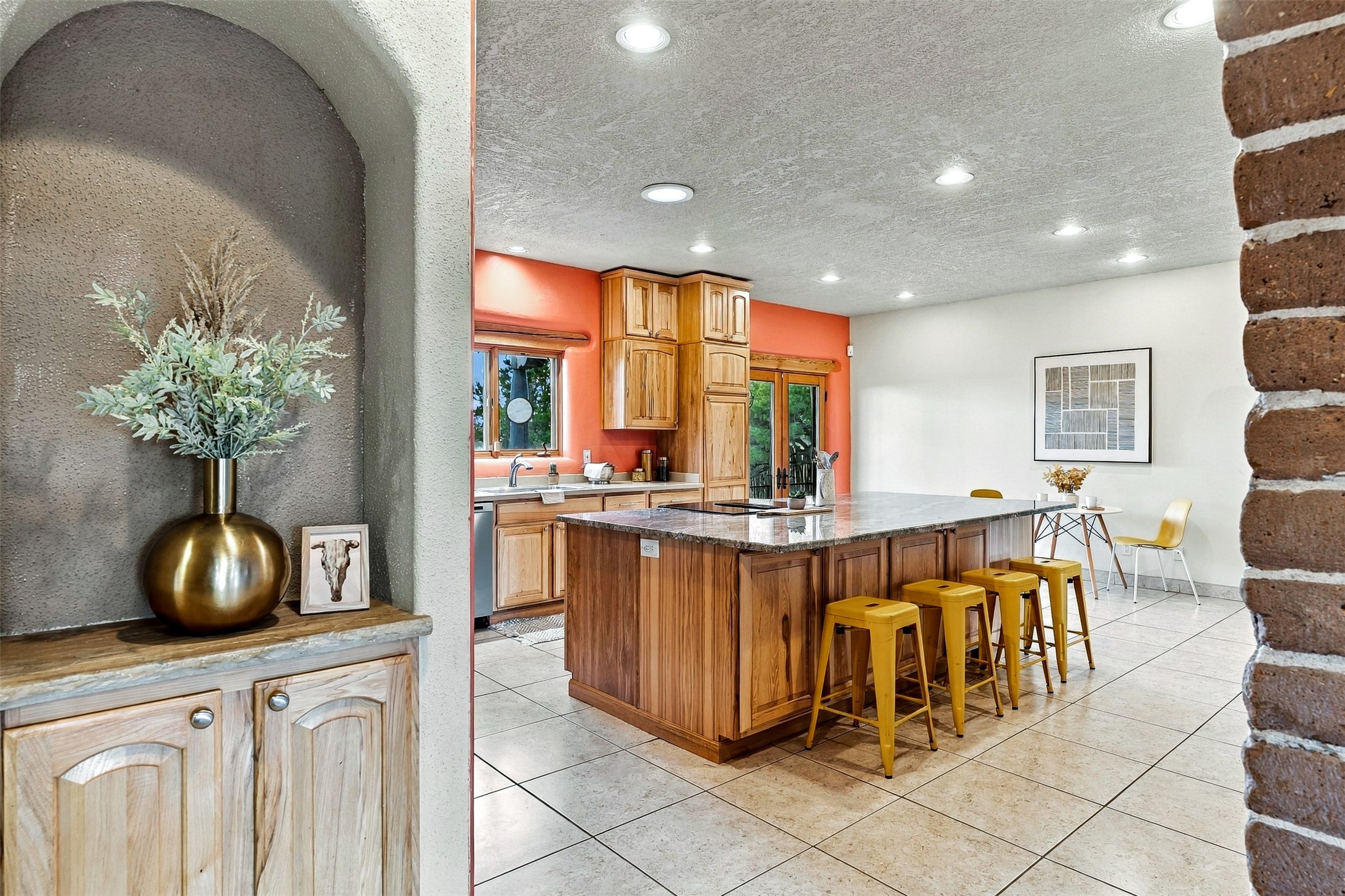 Kitchen with a wood-and-stone island, yellow stools, and coral walls around the sink.