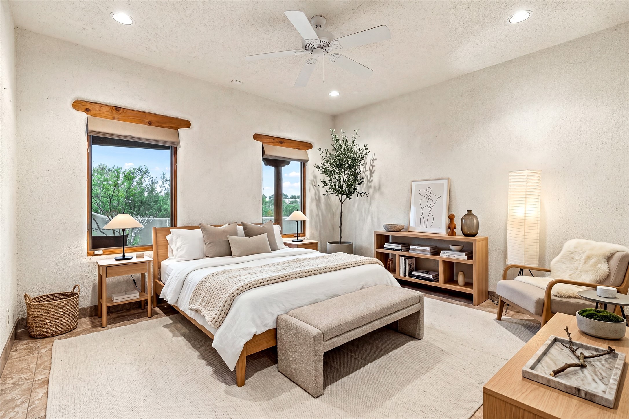 Staged bedroom with a wood-framed bed, woven throw, and windows overlooking leafy trees.