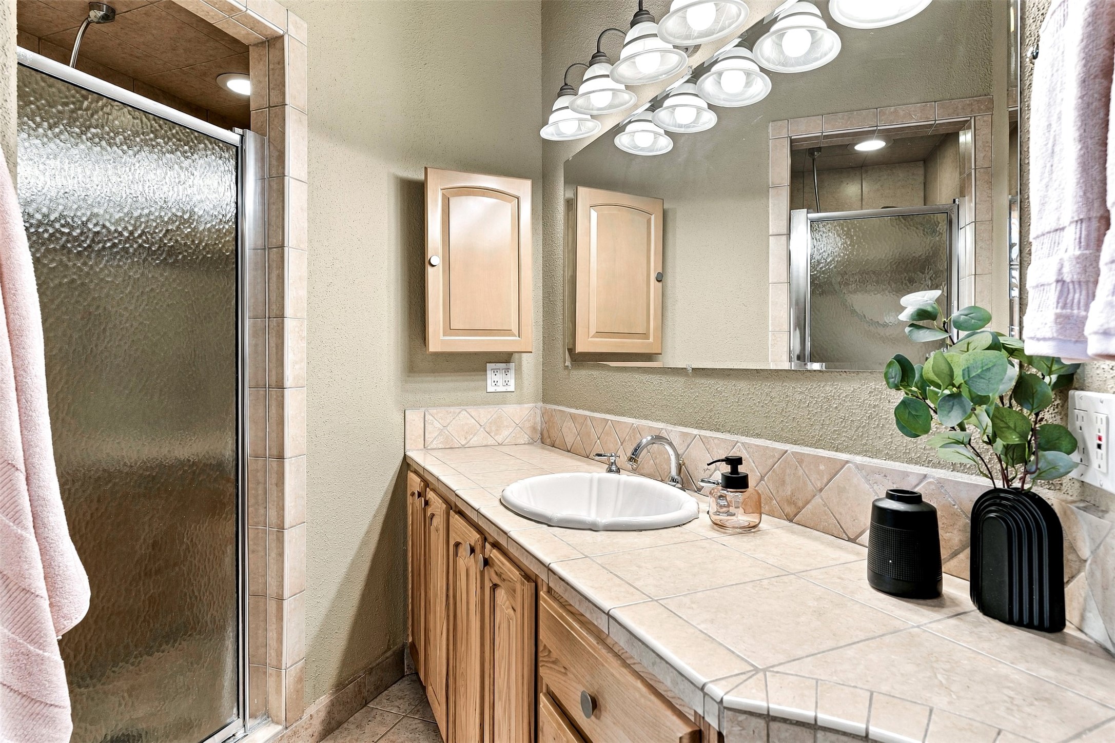 Bathroom with tiled vanity and oval sink beside a glass-enclosed shower.