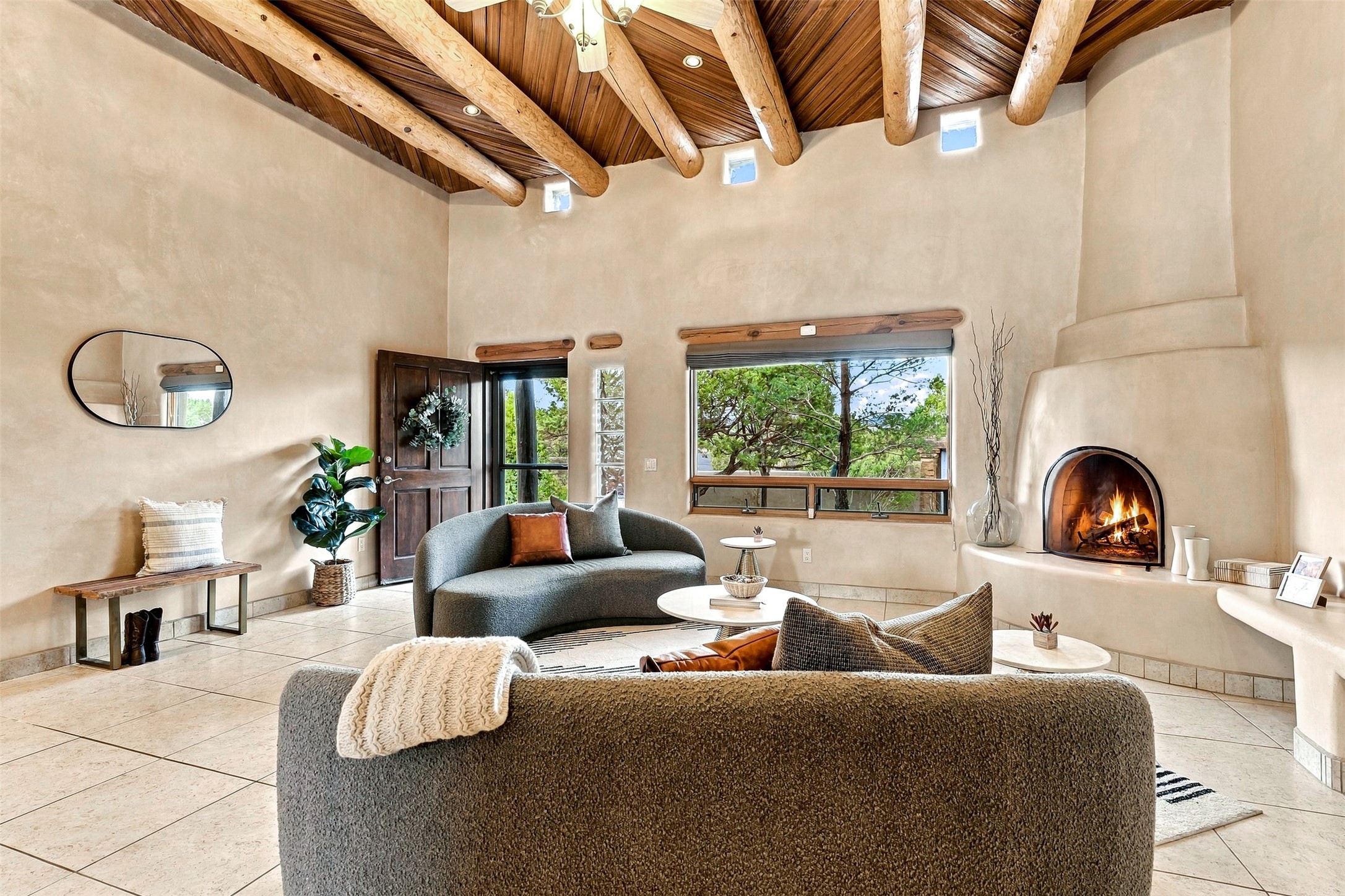 Living room with exposed wood beams, curved sofas, and a lit kiva fireplace.