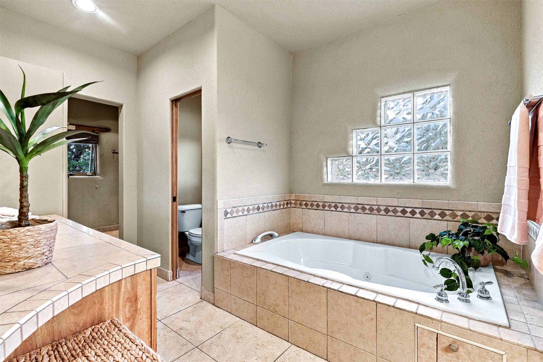 Bathroom with a tiled soaking tub beneath a glass-block window and a tiled vanity.