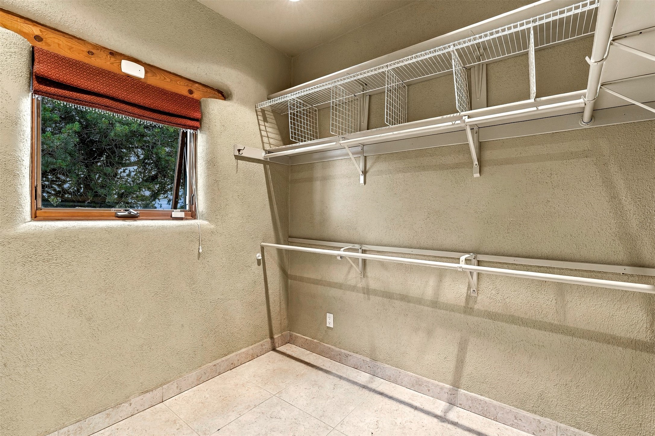 Walk-in closet with extensive wire shelving, tiled floor, and a window with a red shade.