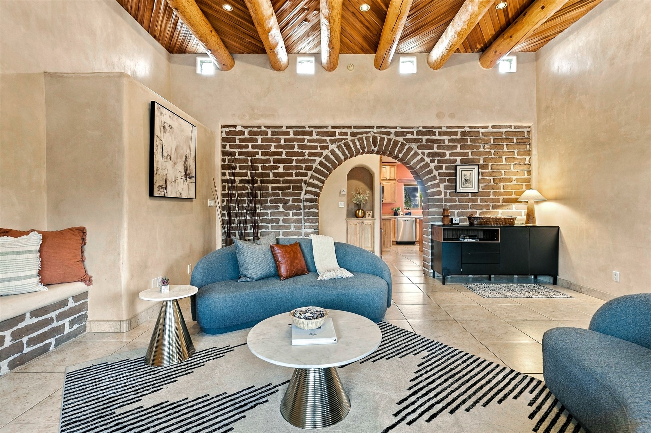 Living room with exposed wood beams, a brick archway, and a curved blue sofa.
