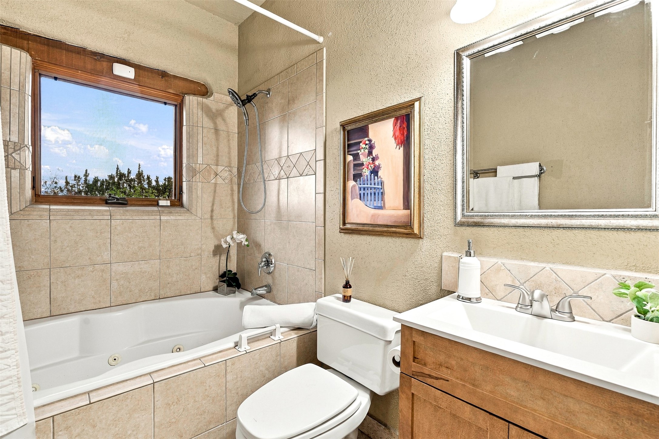 Bathroom with a tiled jetted tub beneath a tree-view window and a wood vanity.