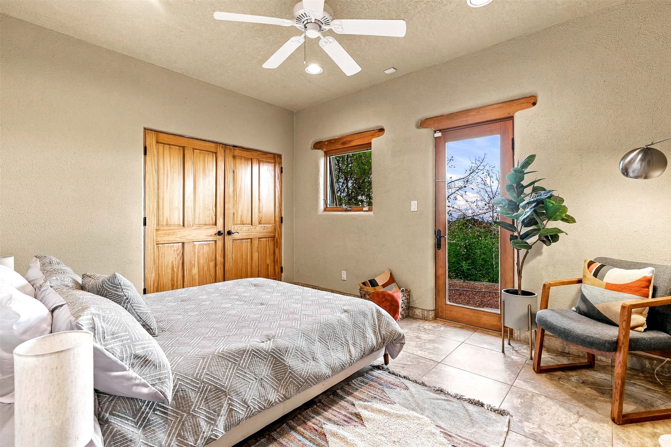 Bedroom with a gray patterned bedspread, rustic wooden doors, and a glass door opening to greenery.