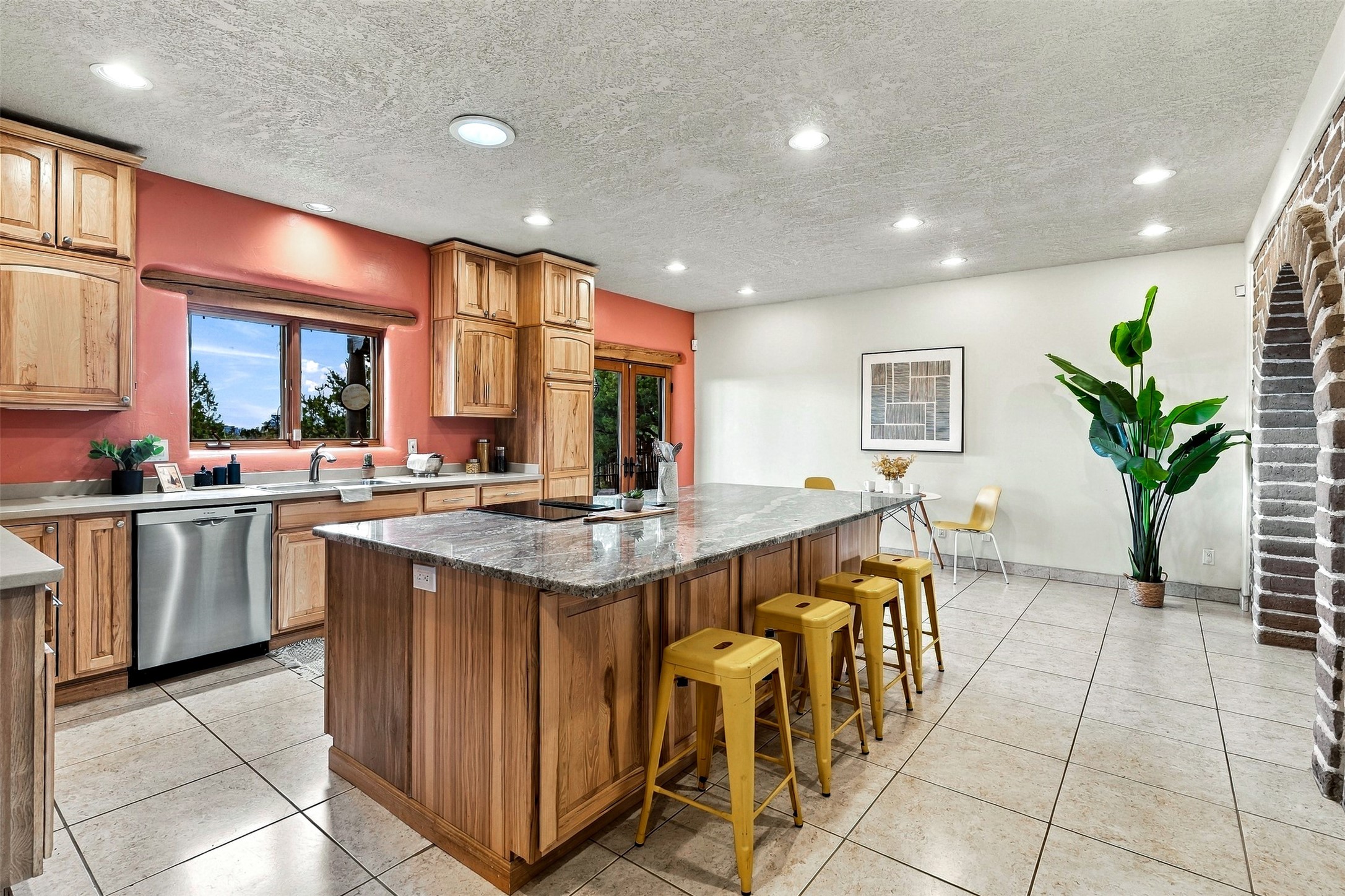 Kitchen with wood cabinets, a broad stone island, yellow stools, and a brick archway.