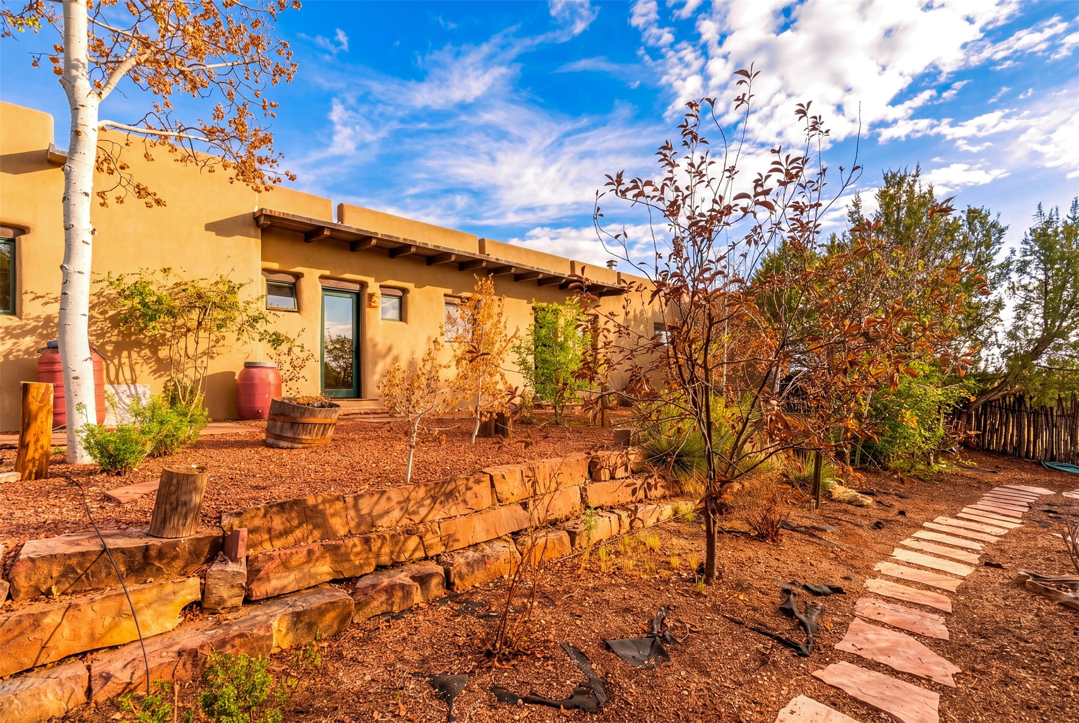 Adobe-style home beside a gravel garden with stone retaining walls and an autumn stepping-stone path.