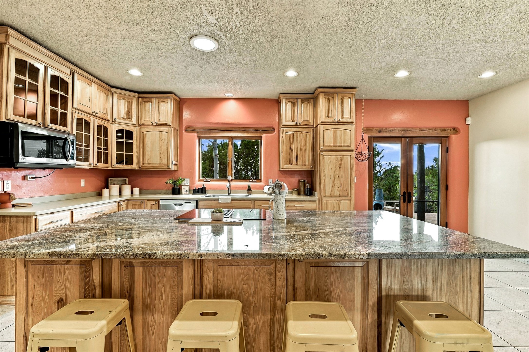 Kitchen with a large granite island, four stools, natural wood cabinets, and coral walls.