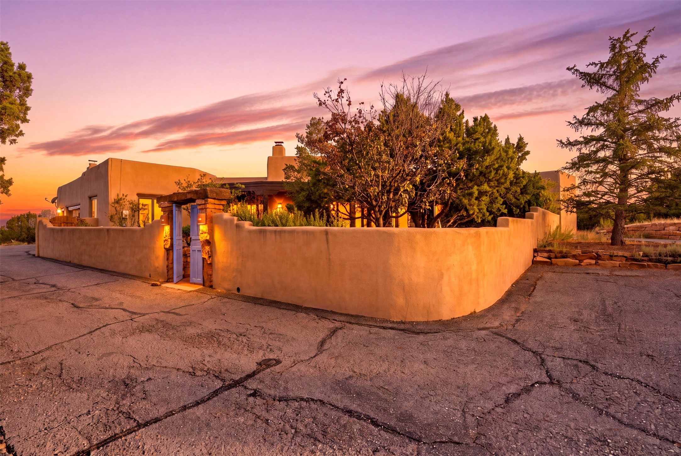 Adobe-style home behind a curved courtyard wall and purple gate at sunset.
