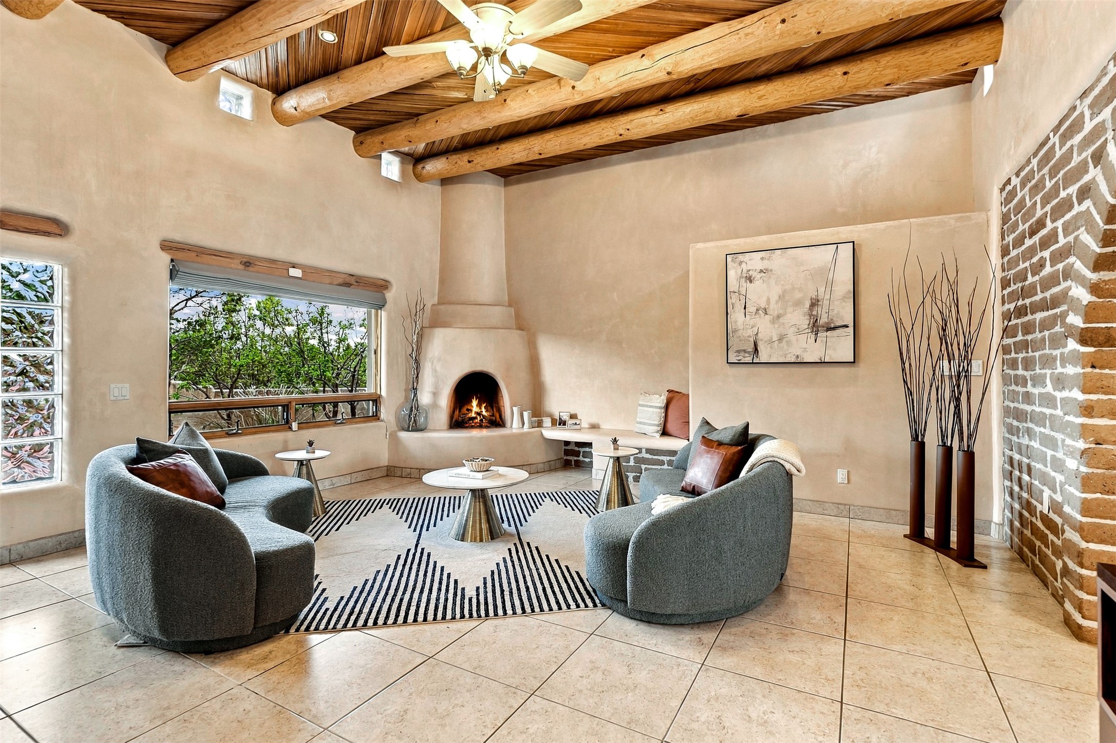Living room with a kiva fireplace, exposed wood beams, and gray lounge chairs on a striped rug.
