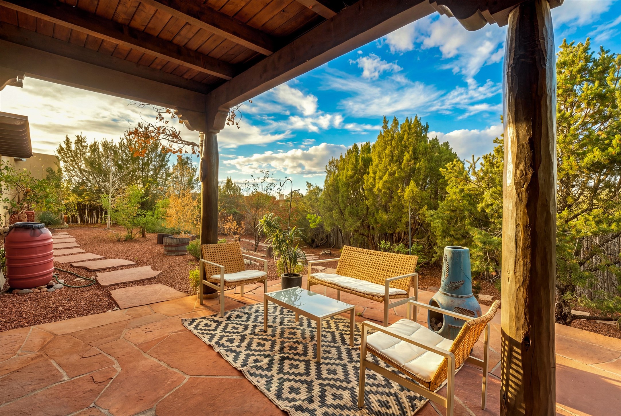 Covered flagstone patio with wicker seating, a blue chiminea, and a landscaped garden.