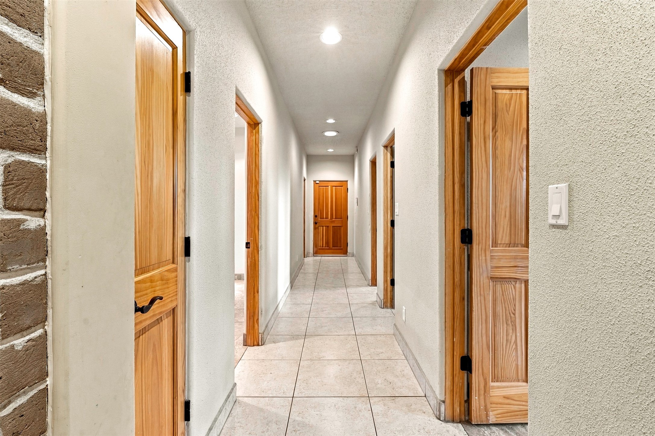 Hallway with tiled floors, warm wood doors, recessed lights, and a stone accent wall.