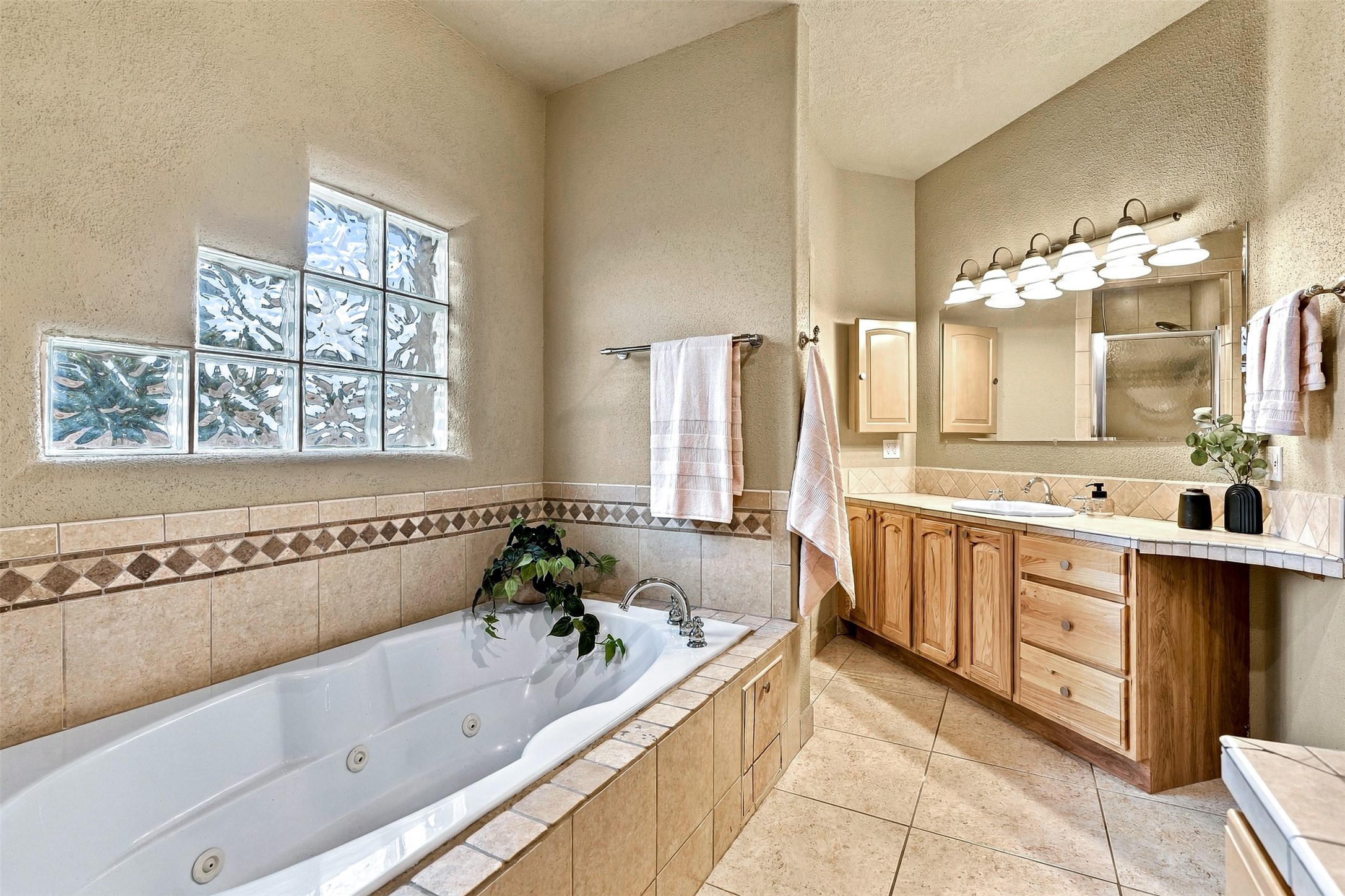 Bathroom with a tiled soaking tub, glass-block window, and wooden vanity.