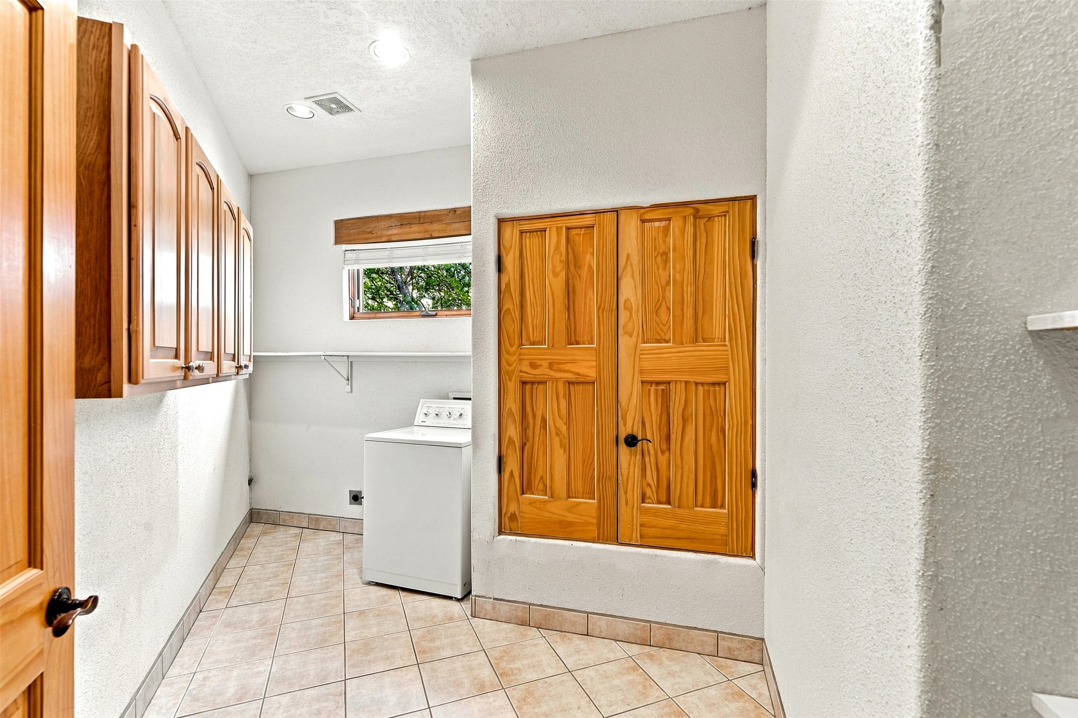 Laundry room with a washing machine, wooden cabinets, and tan tile flooring.