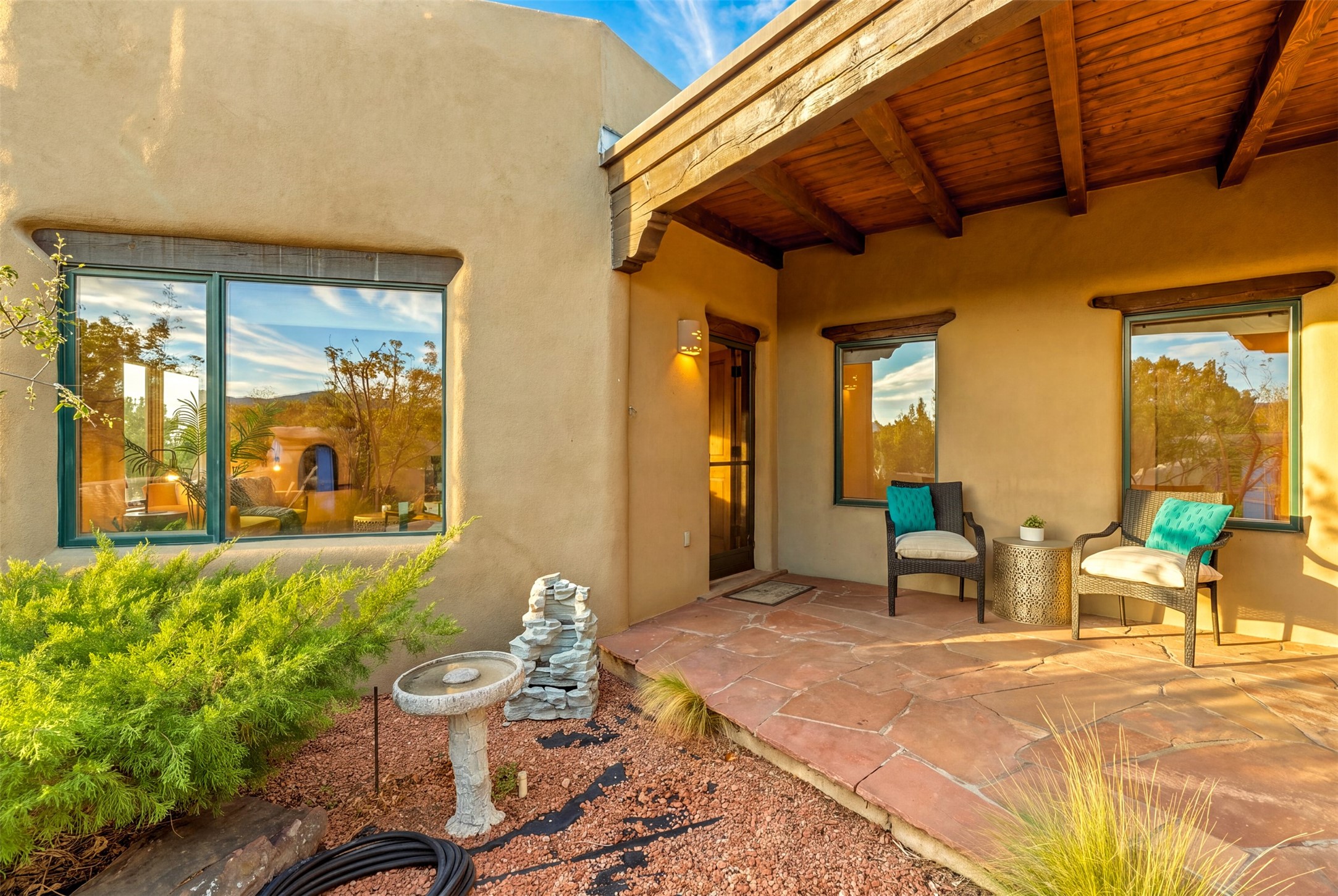 Covered patio with timber ceiling, terracotta tiles, wicker chairs, and desert landscaping.