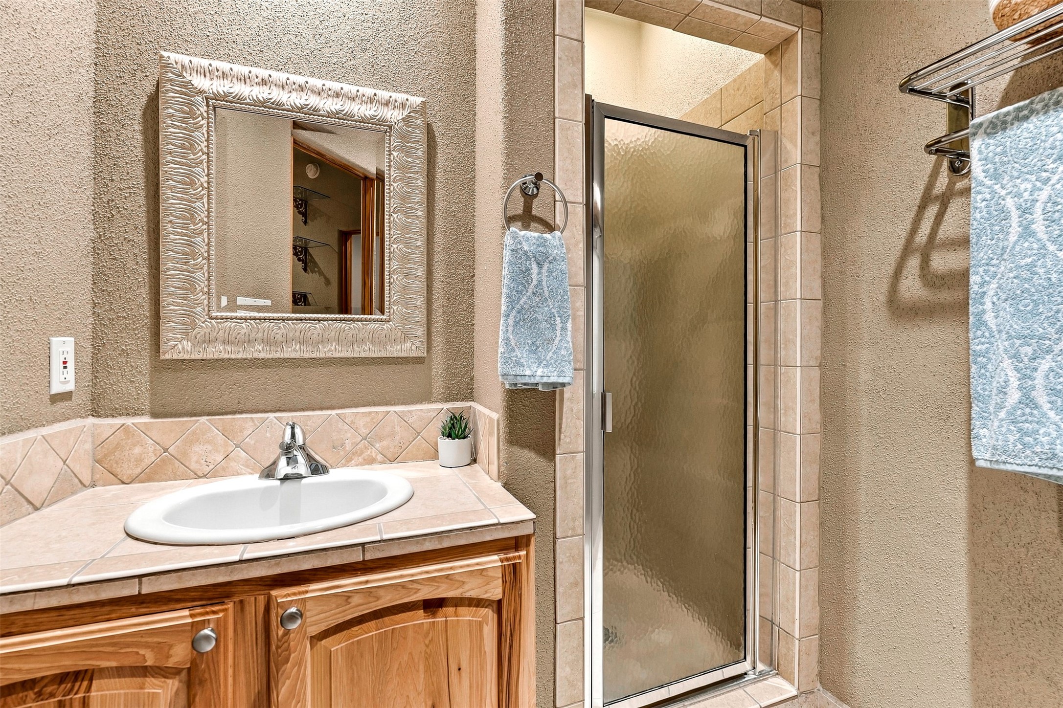 Bathroom with a glass-enclosed shower, tiled vanity, wood cabinetry, and ornate mirror.