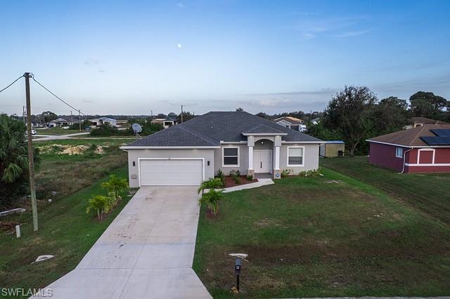 Aerial view of a gray single-story home with an attached garage and long concrete driveway.