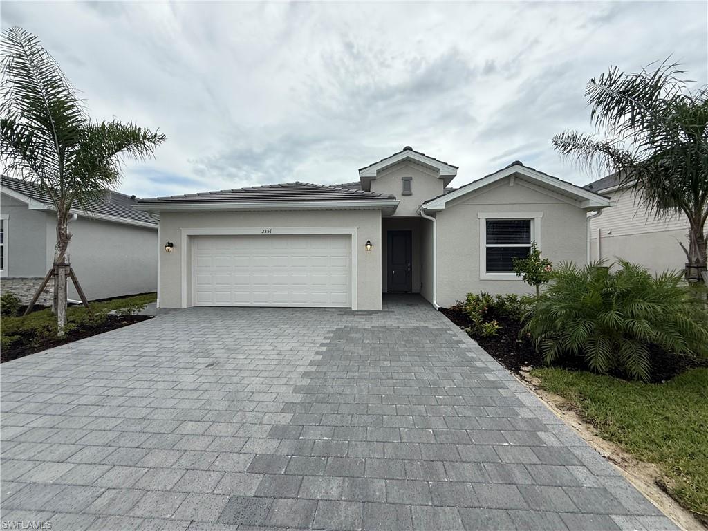 Single-story home with a wide paver driveway, two-car garage, and palm trees.