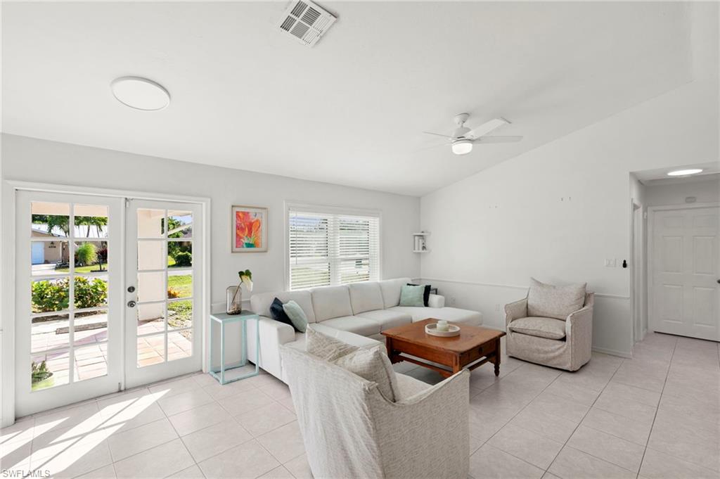 Living room with a white sectional, upholstered chairs, and French doors opening to a sunny patio.