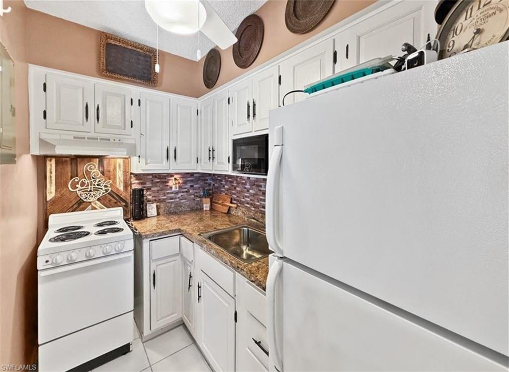 Compact kitchen with white cabinetry, brown countertops, a tile backsplash, and white appliances.