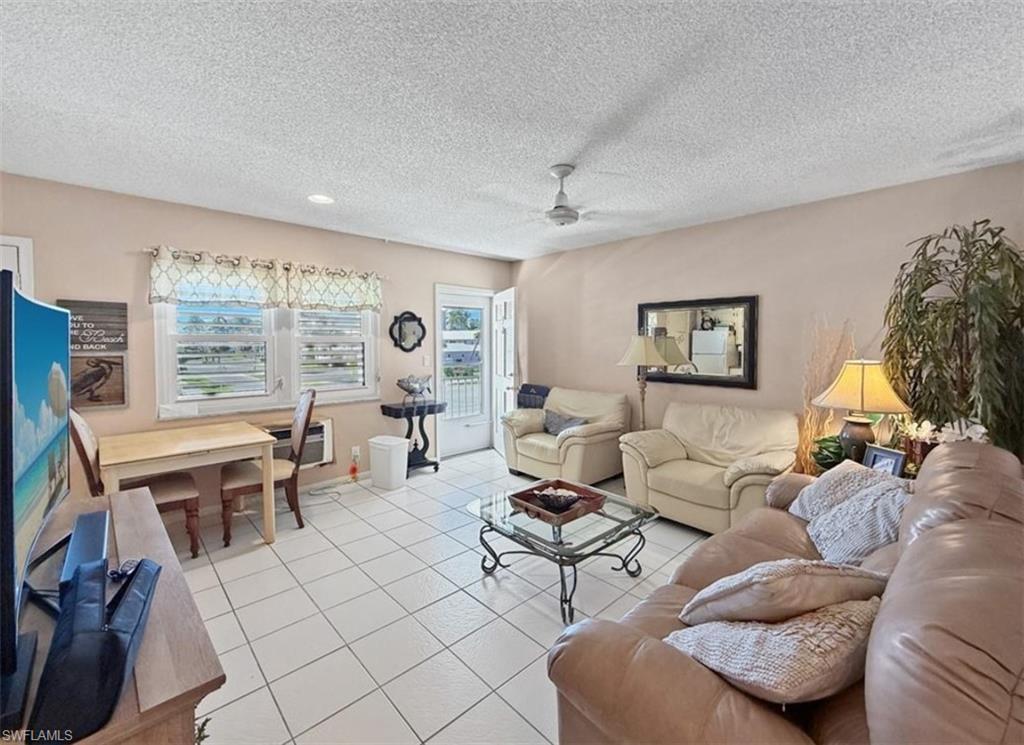 Living room with beige seating, a glass coffee table, tiled floors, and an open door beside the windows.