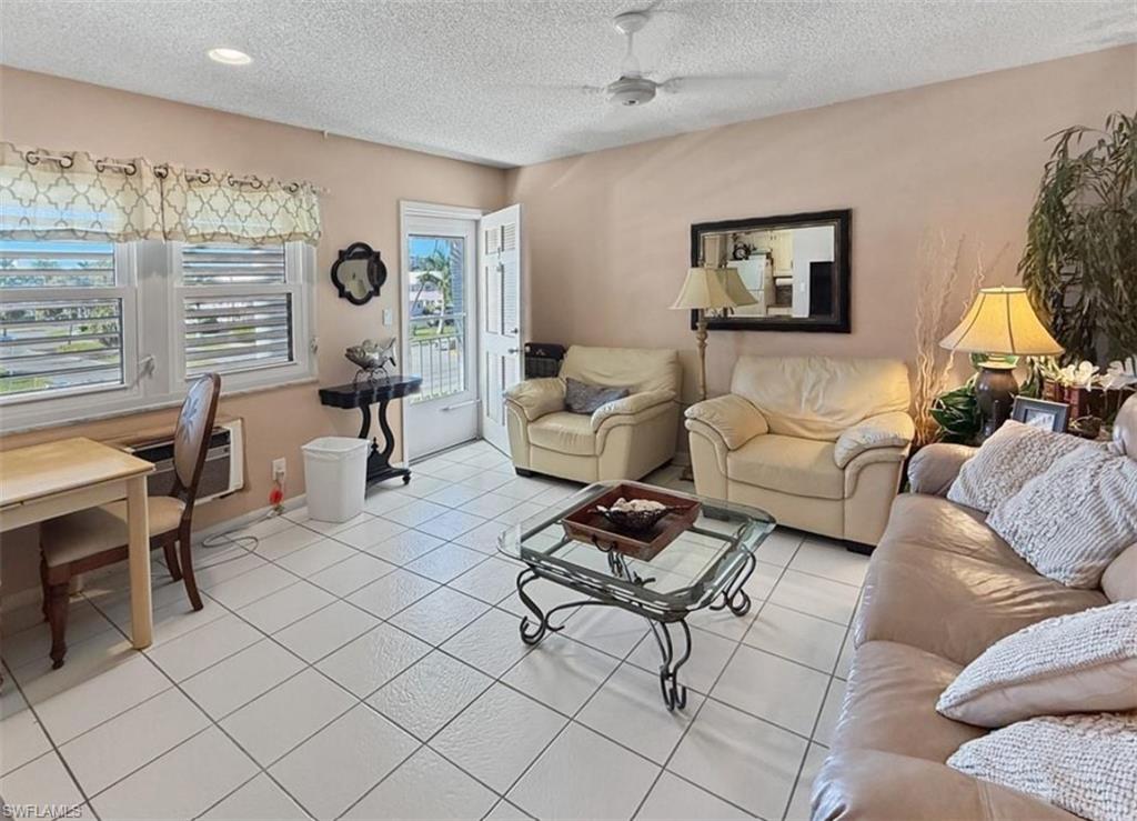 Living room with cream sofas, glass coffee table, white tile floors, and an open balcony door.