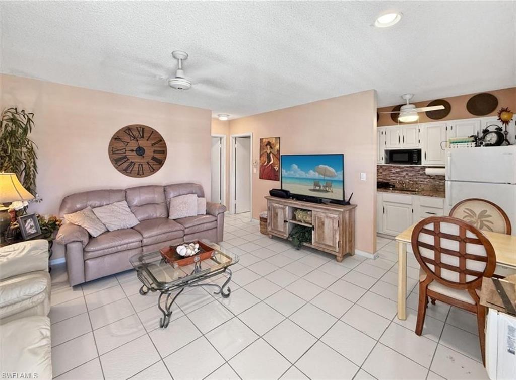 Furnished living and dining area with a gray sofa, glass coffee table, and compact white kitchen.