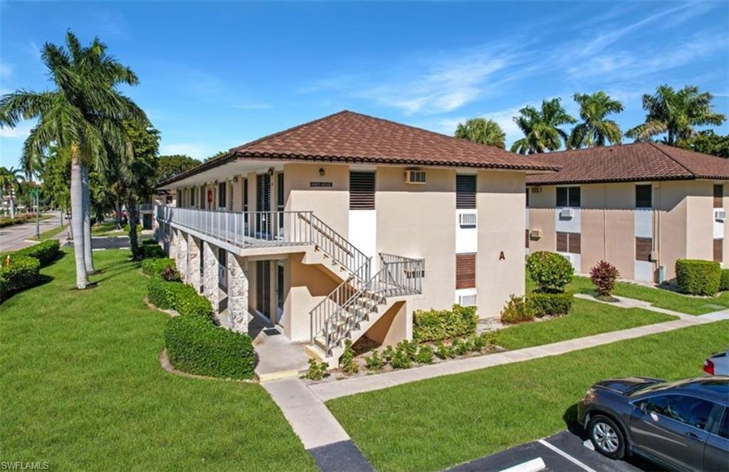 Condominium building with a red tile roof, exterior stairs, and palm trees along the lawn.