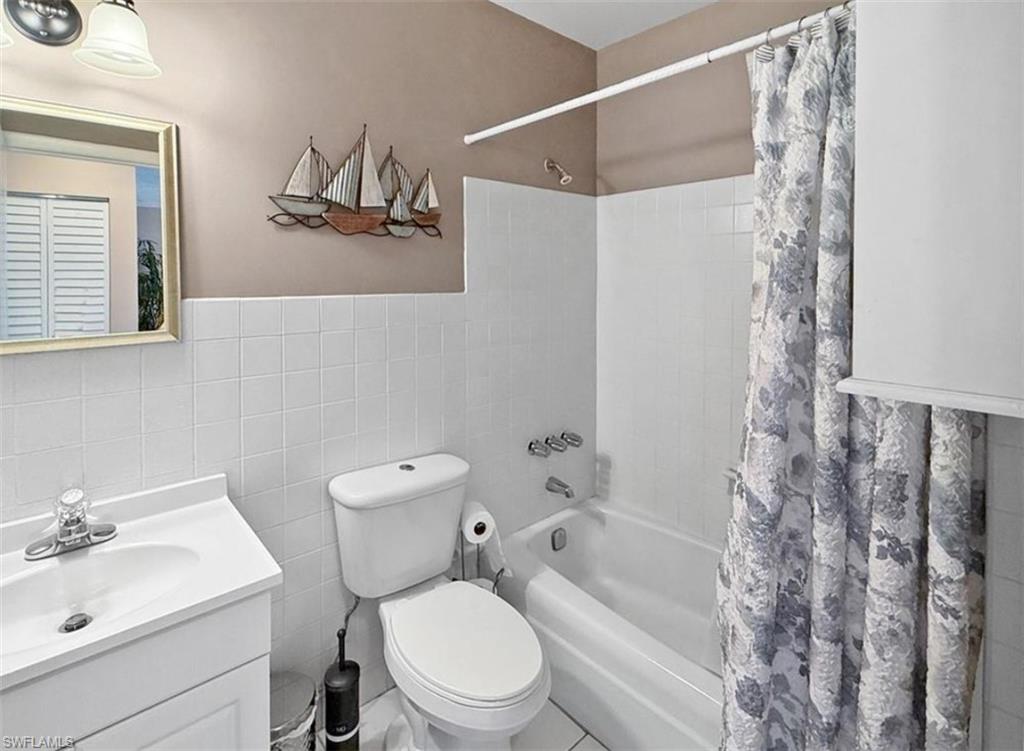 Bathroom with a white vanity, toilet, and bathtub behind a patterned shower curtain.