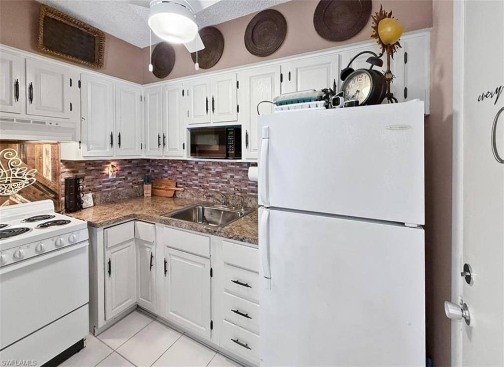Kitchen with white cabinets and appliances, speckled countertops, and a brown mosaic backsplash.