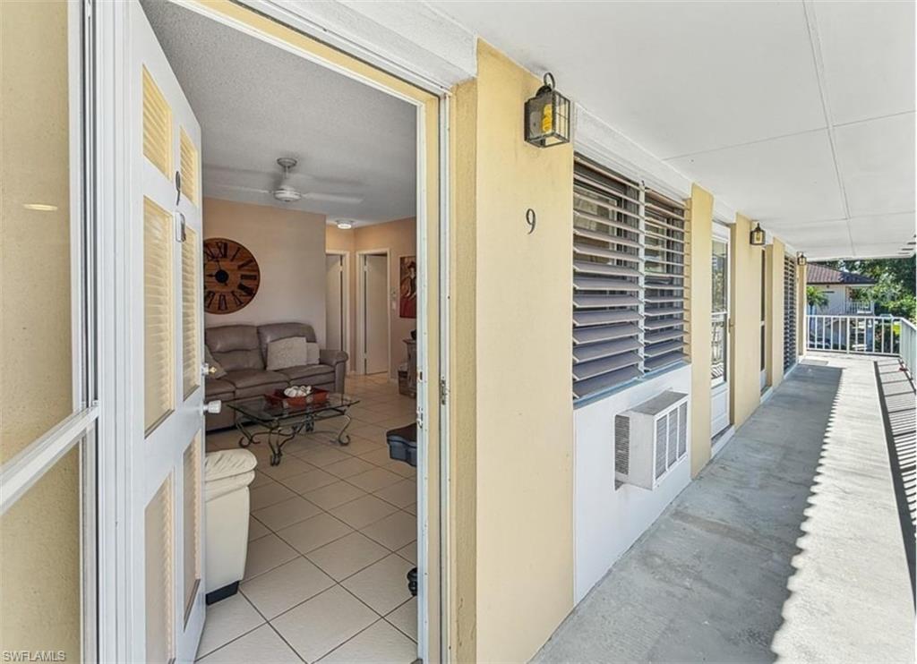 Condo entrance along a covered walkway, with an open door revealing a tiled living room.