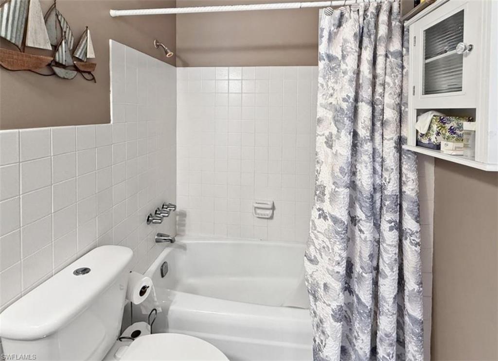 Bathroom with a white tiled bathtub and gray-and-white patterned shower curtain.