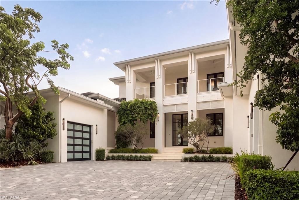 Modern white two-story home with columned balconies, landscaped entry, and broad paved driveway.