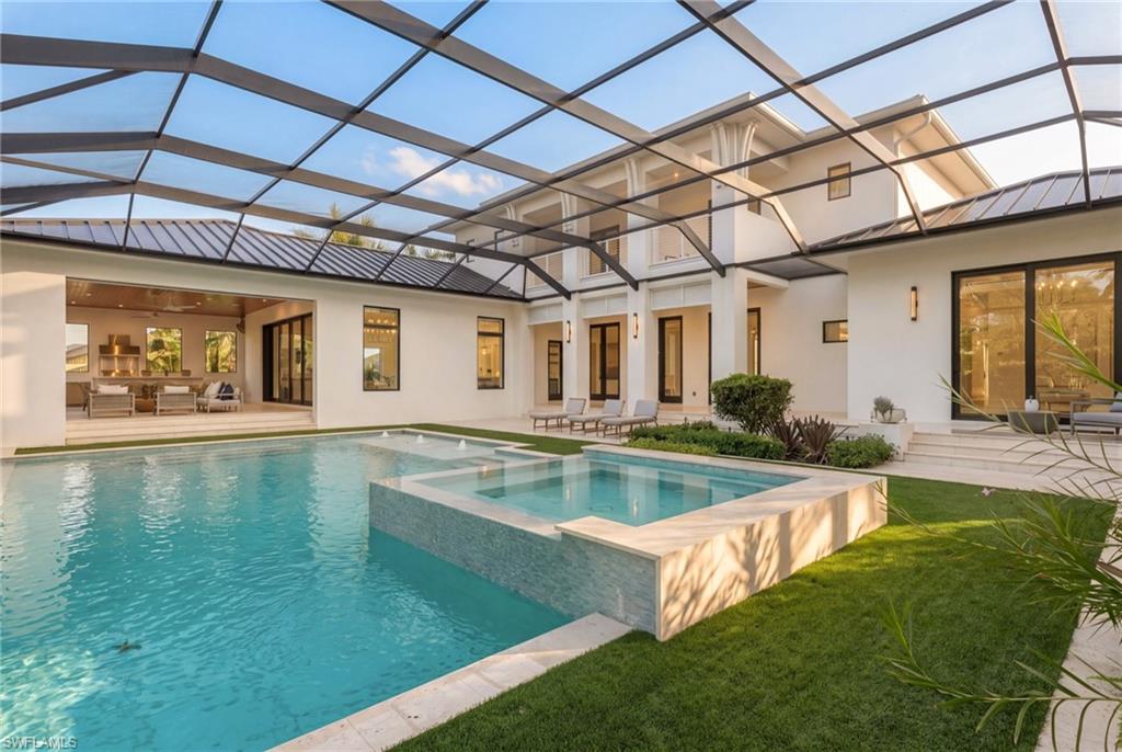 Courtyard pool and raised spa beneath a screened enclosure, with the home and furnished seating beyond.