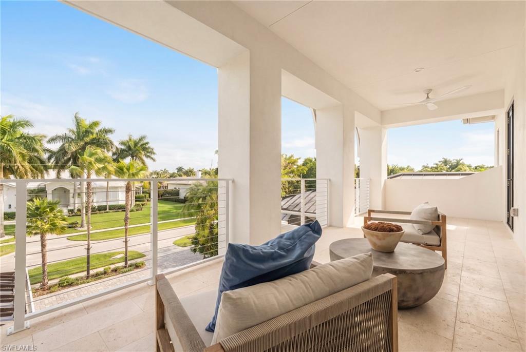 Covered balcony with lounge seating overlooking a palm-lined street.