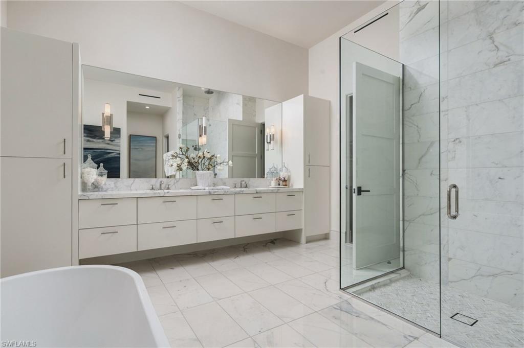 Bathroom with a double vanity, marble surfaces, glass shower, and freestanding tub.