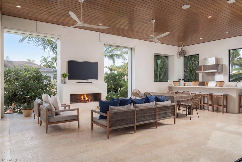 Open living room and kitchen with a fireplace, blue seating, and a wood-plank ceiling.
