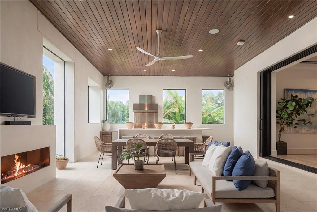 Living room and dining area with a wood-plank ceiling, fireplace, and views of tropical greenery.