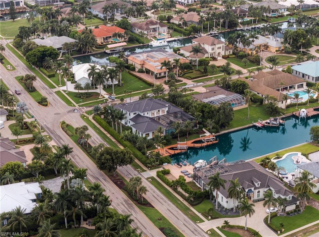 Aerial view of canal-front homes with docks, palm trees, and a nearby road.