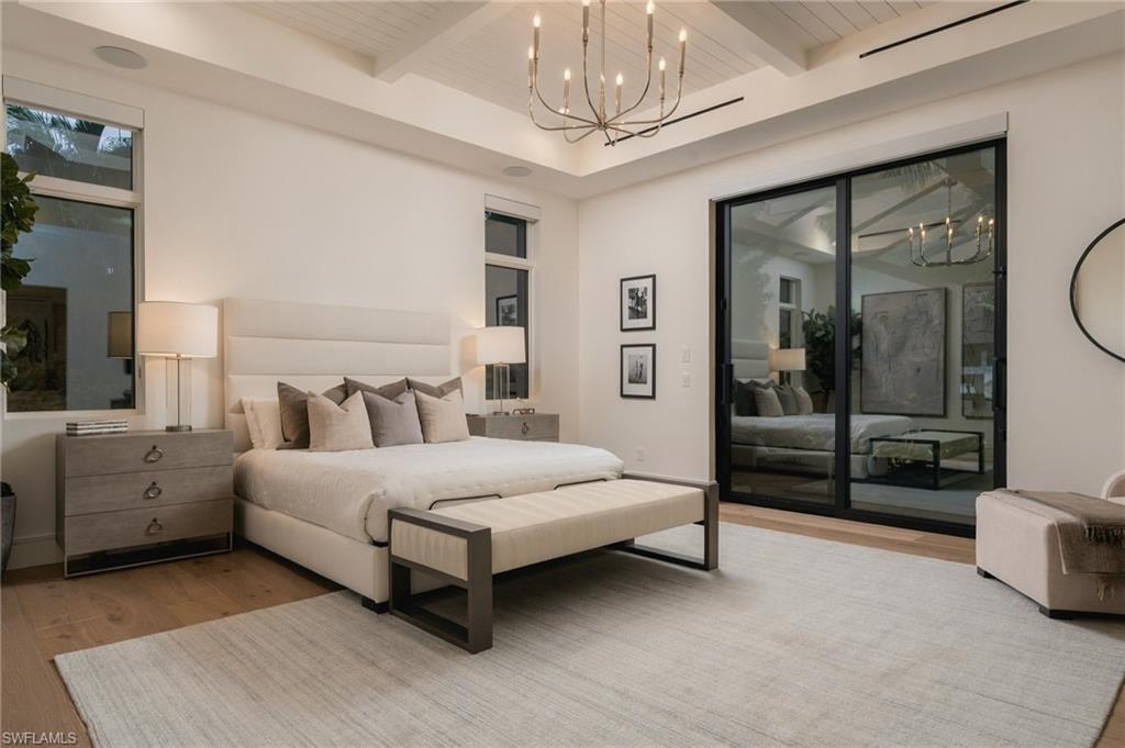 Primary bedroom with a king bed, vaulted beamed ceiling, and black-framed glass doors.