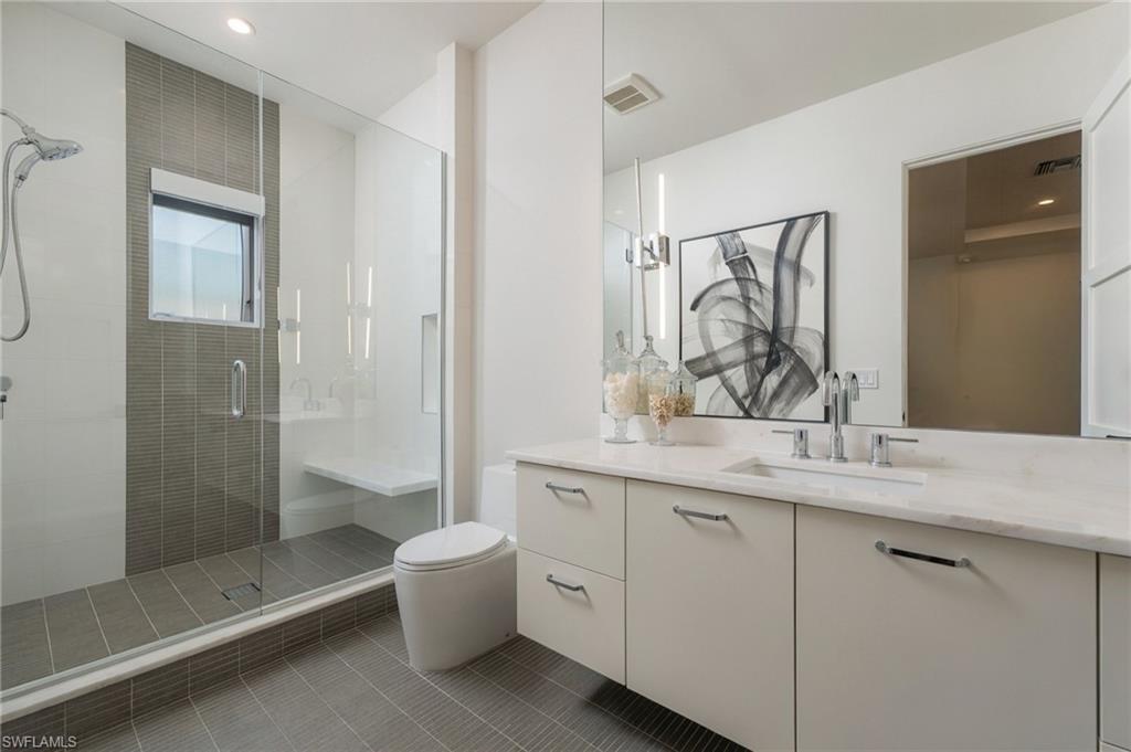 Bathroom with a glass-enclosed shower, gray tile, and a white vanity beneath a large mirror.
