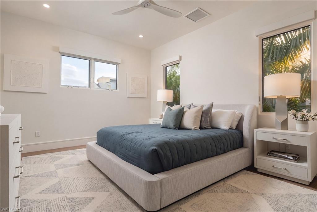 Bright staged bedroom with a king bed, blue quilt, and palm views through the windows.