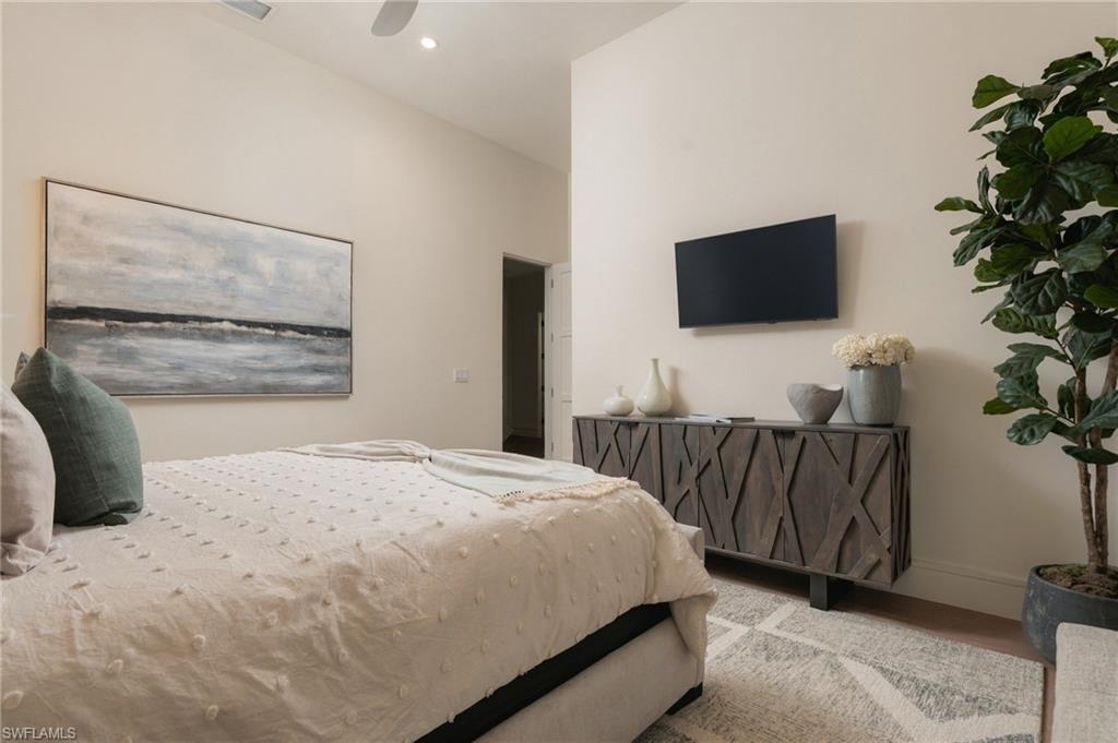 Staged bedroom with a cream bed, abstract seascape, and wall-mounted television above a wood console.
